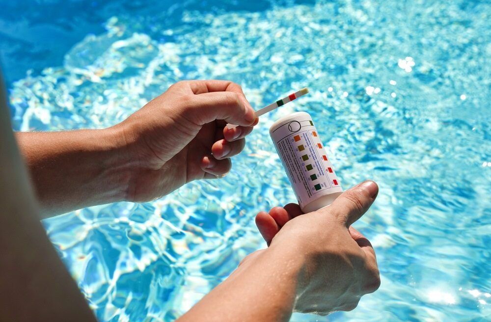 Hands Testing Pool Water With a Color-coded Strip — Dean Thomas Pools in Palm Cove, QLD