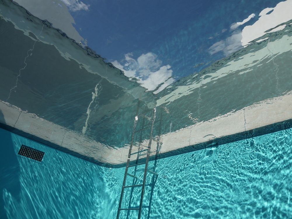 Underwater View of a Pool With a Ladder, Reflecting a Blue Sky With Clouds — Dean Thomas Pools in Tablelands, QLD