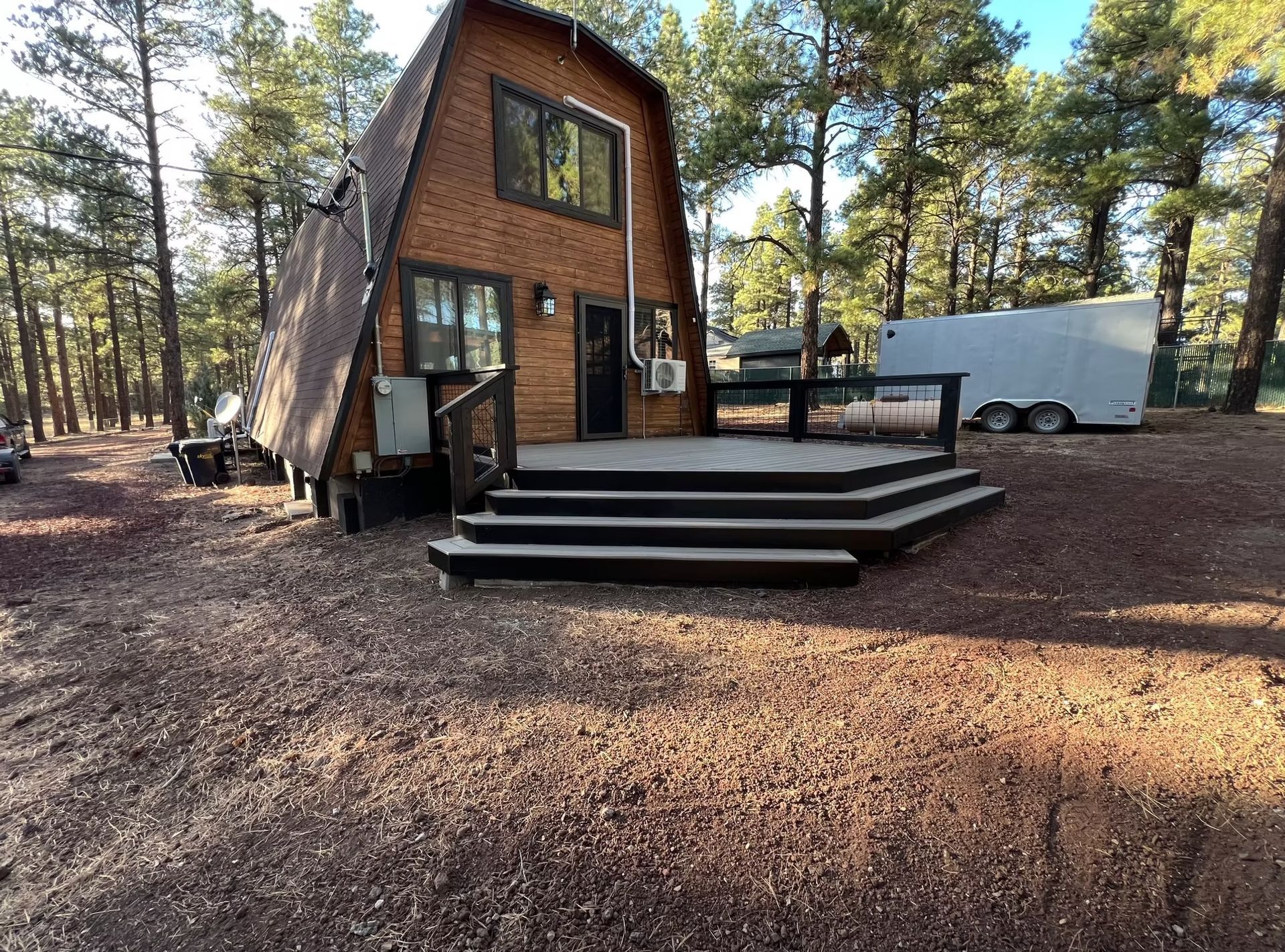 A small house with a deck and stairs in the middle of a forest.