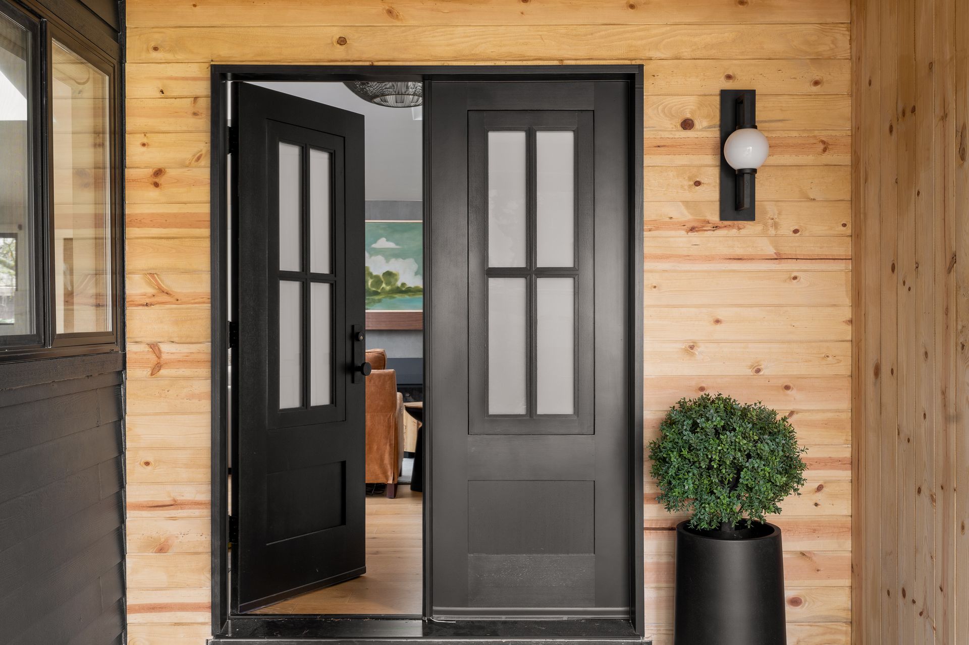 A black door in a wood clad entry with  a potted plant in Seattle, WA.