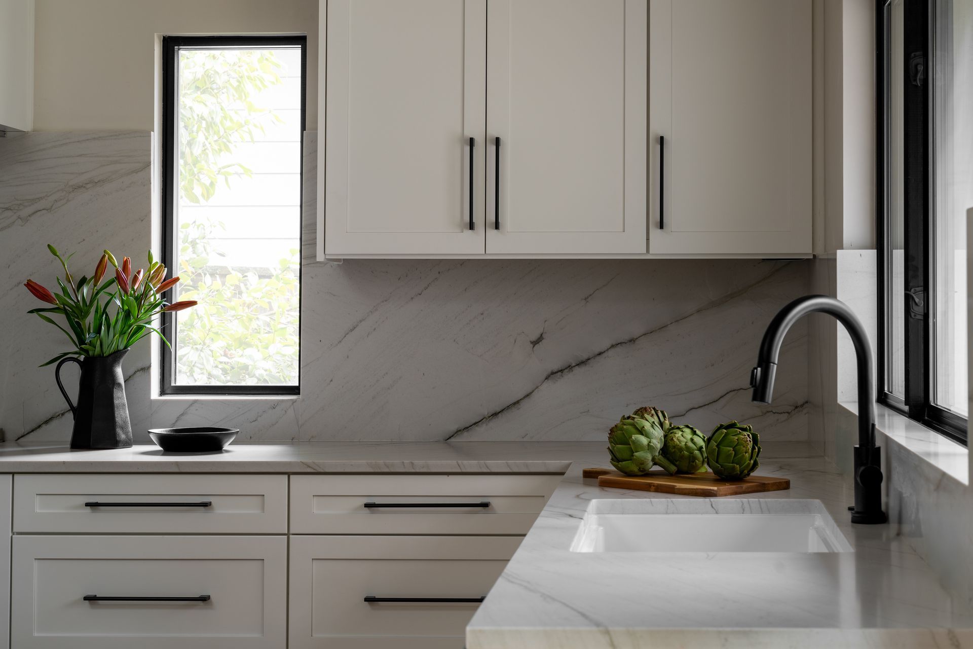 A kitchen with white cabinets , a sink , marble backsplash, and a window in Seattle, WA. 