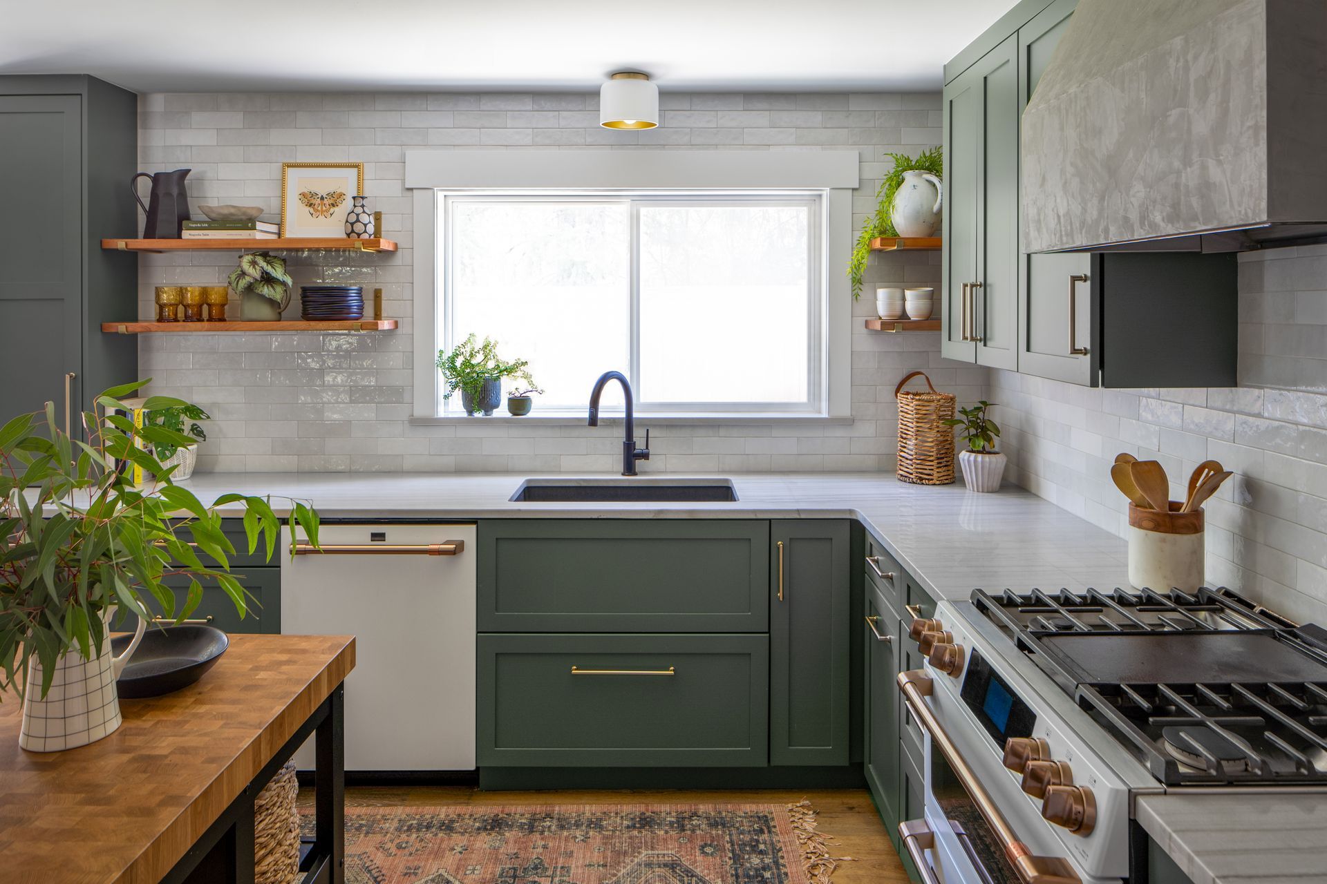 A kitchen with green cabinets , a stove, sink , and window in Seattle, WA. Allison Myers Design. Emily Barrows Photography. 