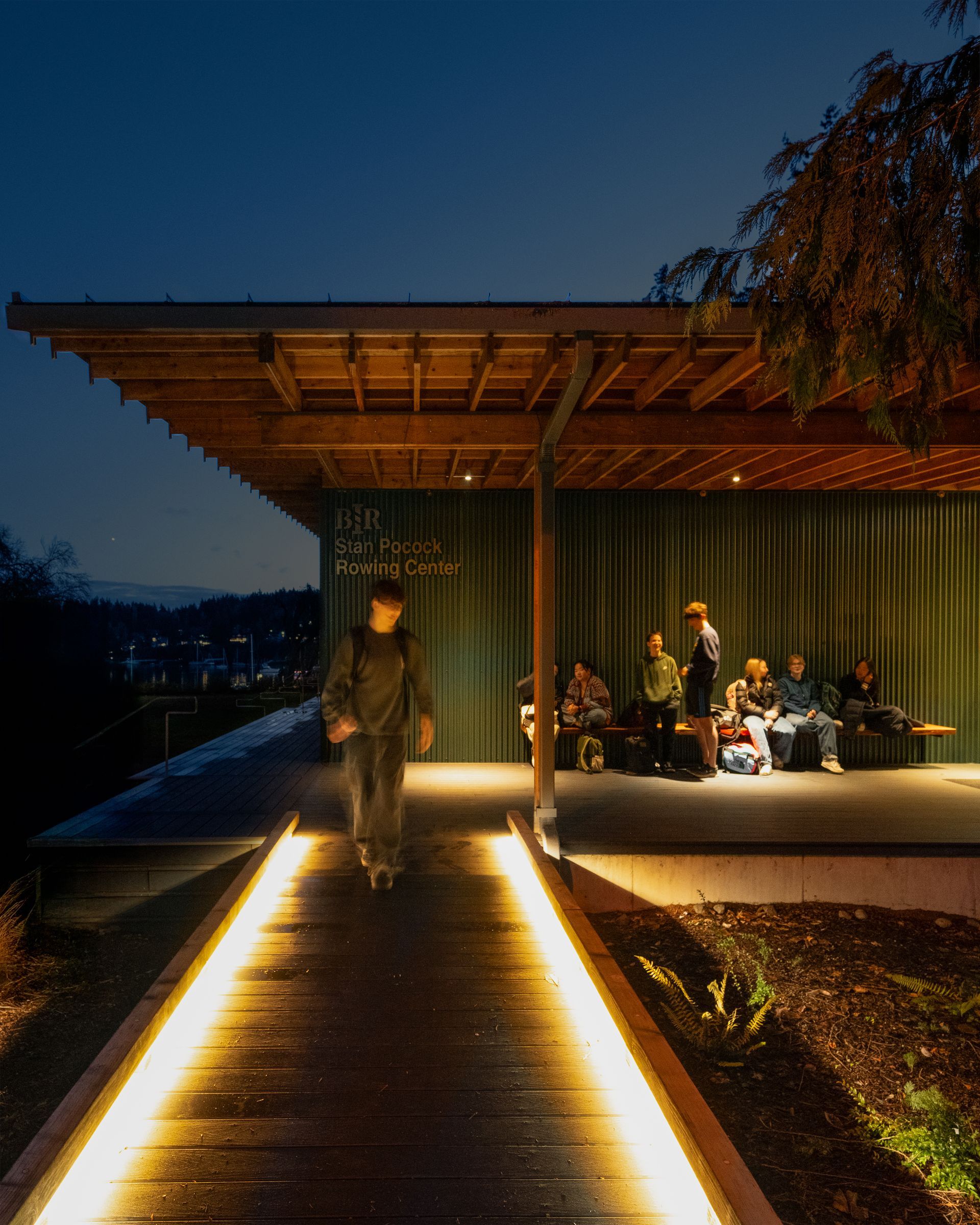 People sitting on a porch at night. Bainbridge Island Rowing Center, Cutler Anderson Architects.  Emily Barrows Photography.