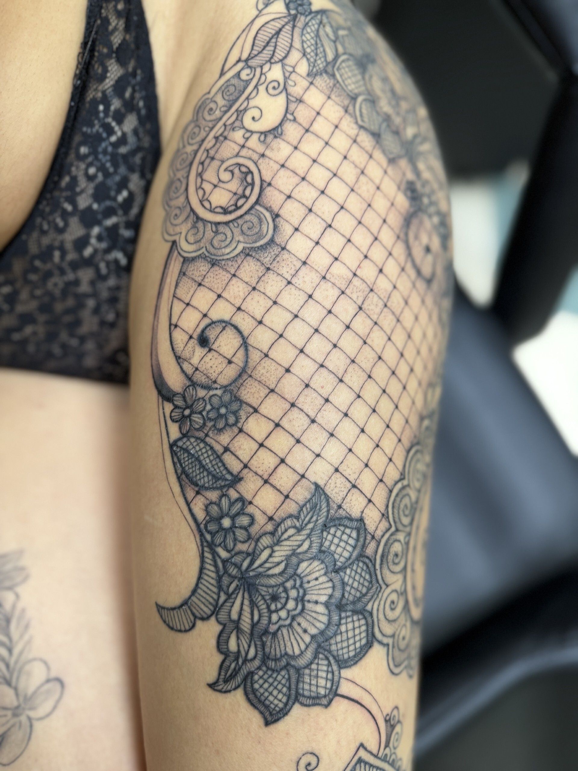 Gamba con intricato tatuaggio floreale e a forma di cuore in bianco e nero, piede su pavimento a scacchi.