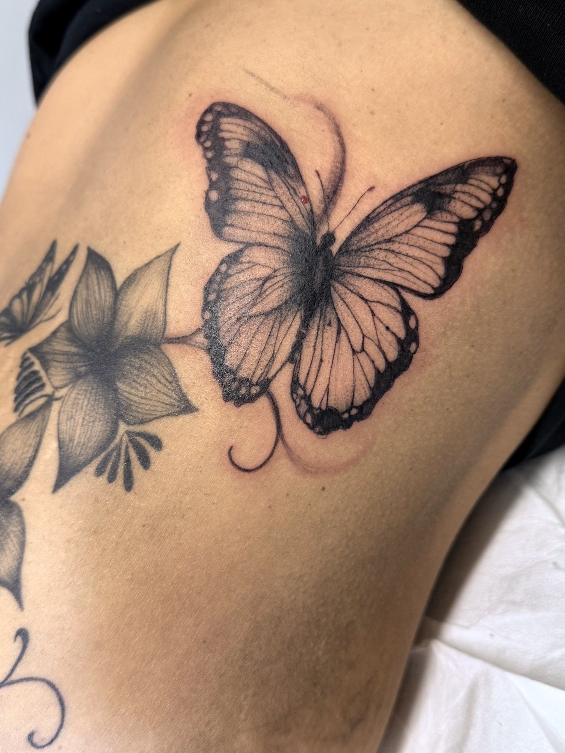 Tatuaggio sulla pelle raffigurante una farfalla e un fiore neri e grigi.