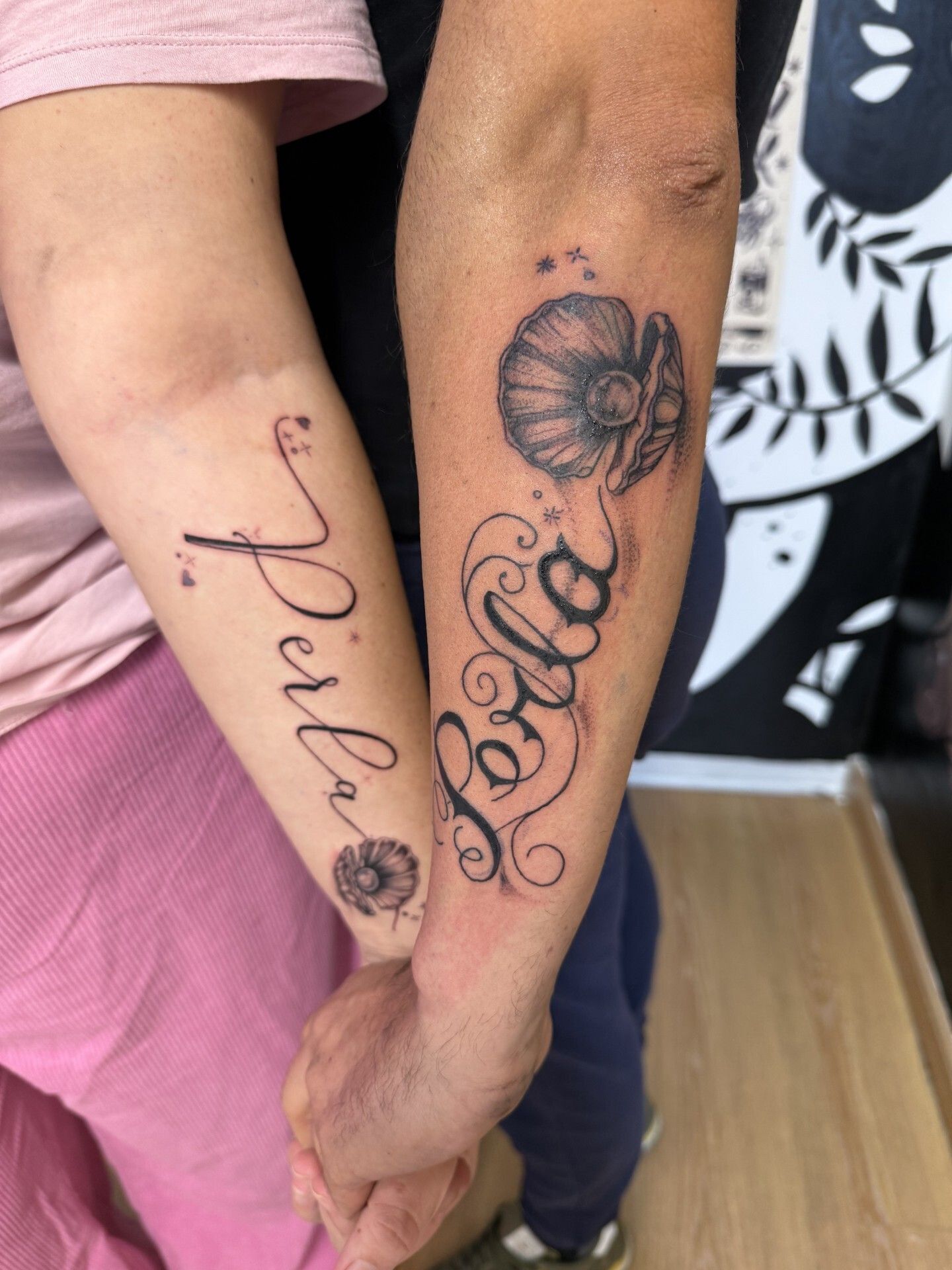 Due braccia affiancate mostrano tatuaggi coordinati: il nome stilizzato