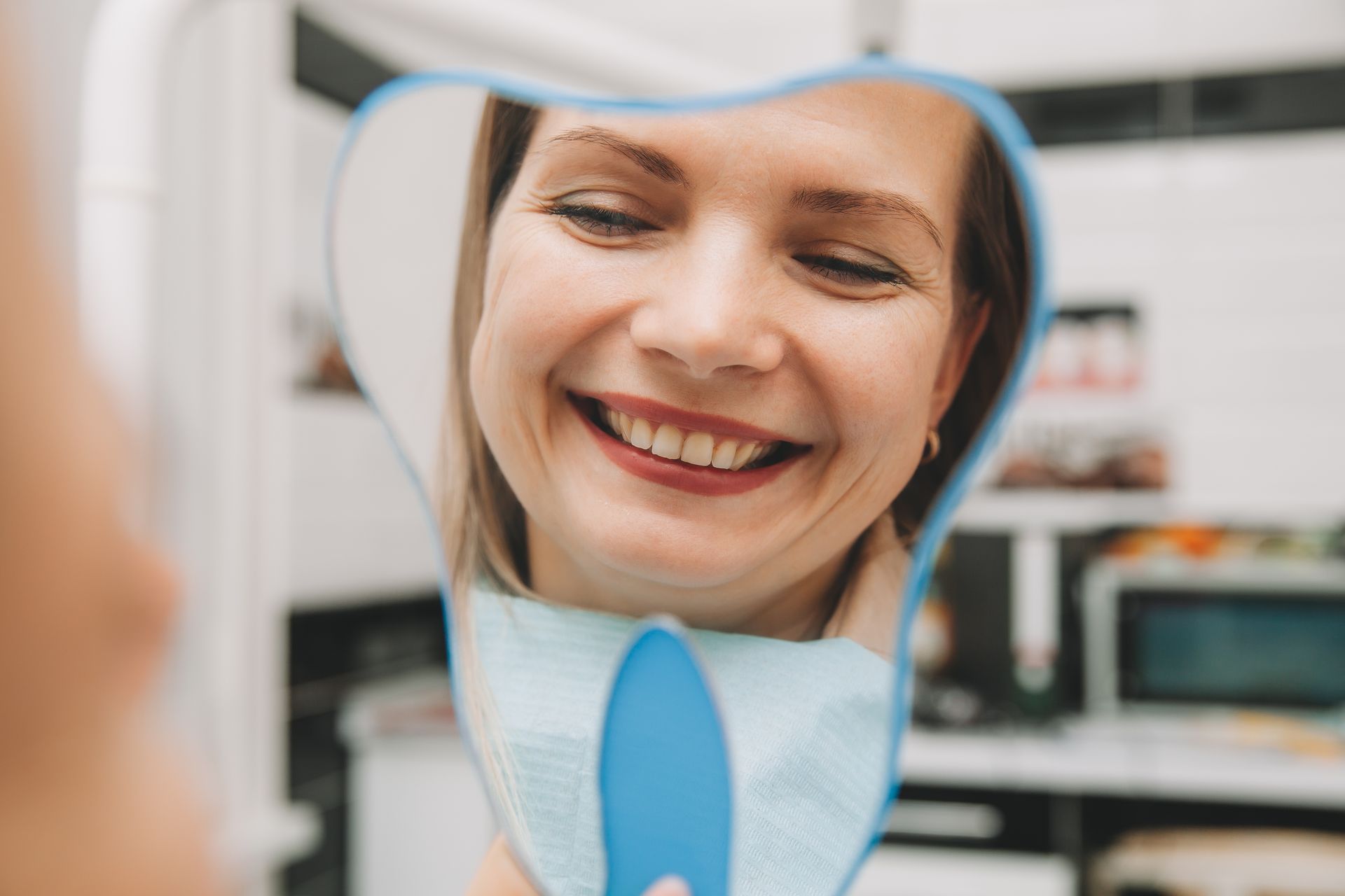 woman looking in the mirror smiling | Teeth cleaning services in Waterford, MI, help maintain oral health.