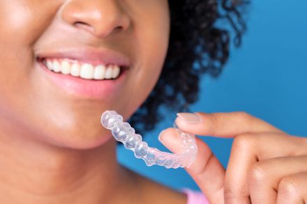 woman smiling holding Invisalign clear aligners | smile makeover near Waterford MI