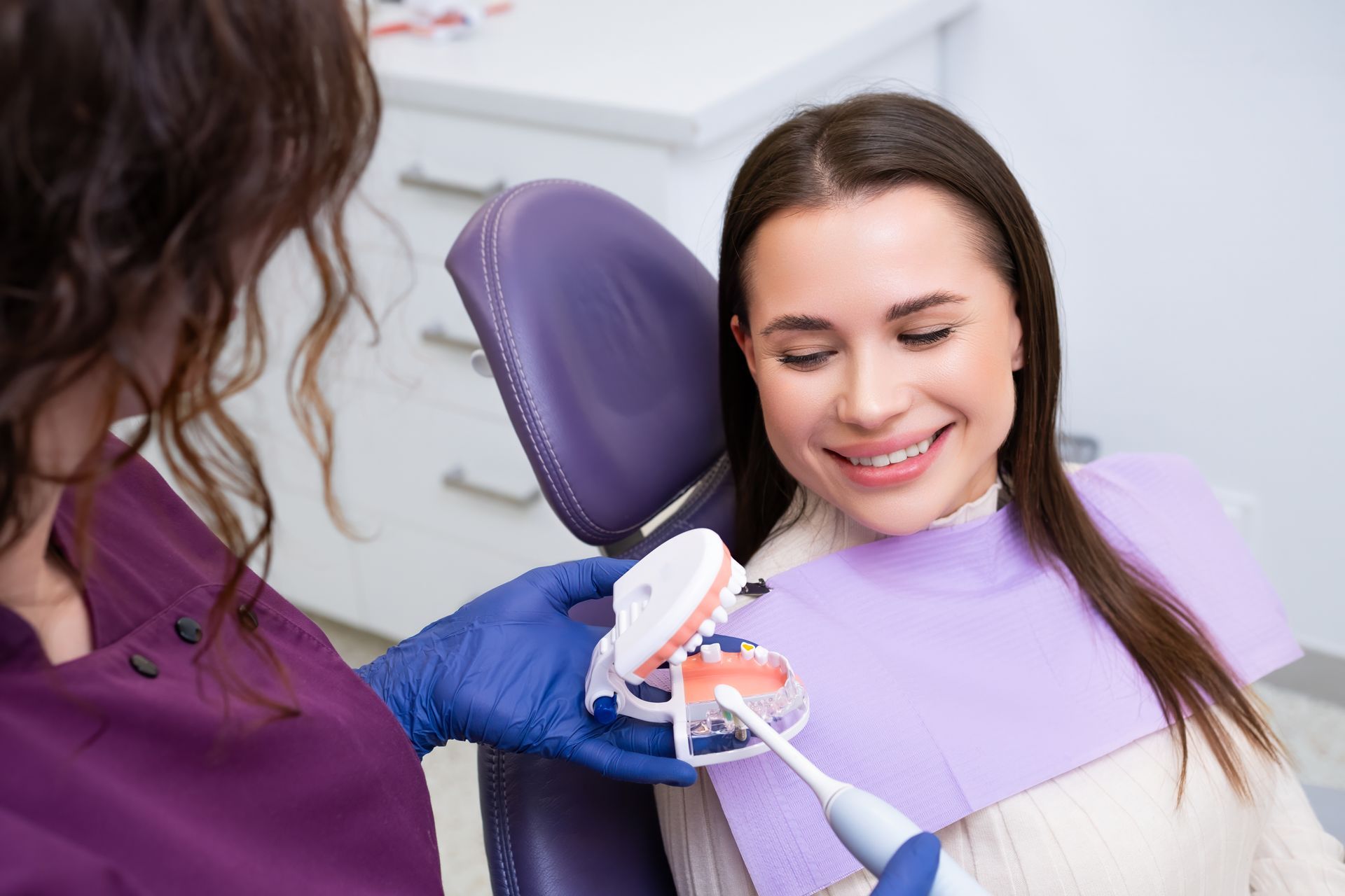 A woman is sitting in a dental chair while a dentist shows her a model of her teeth.