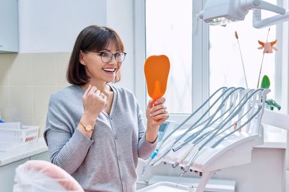 woman smiling at dentist office looking in mirror | teeth cleaning and dentures in Waterford MI 