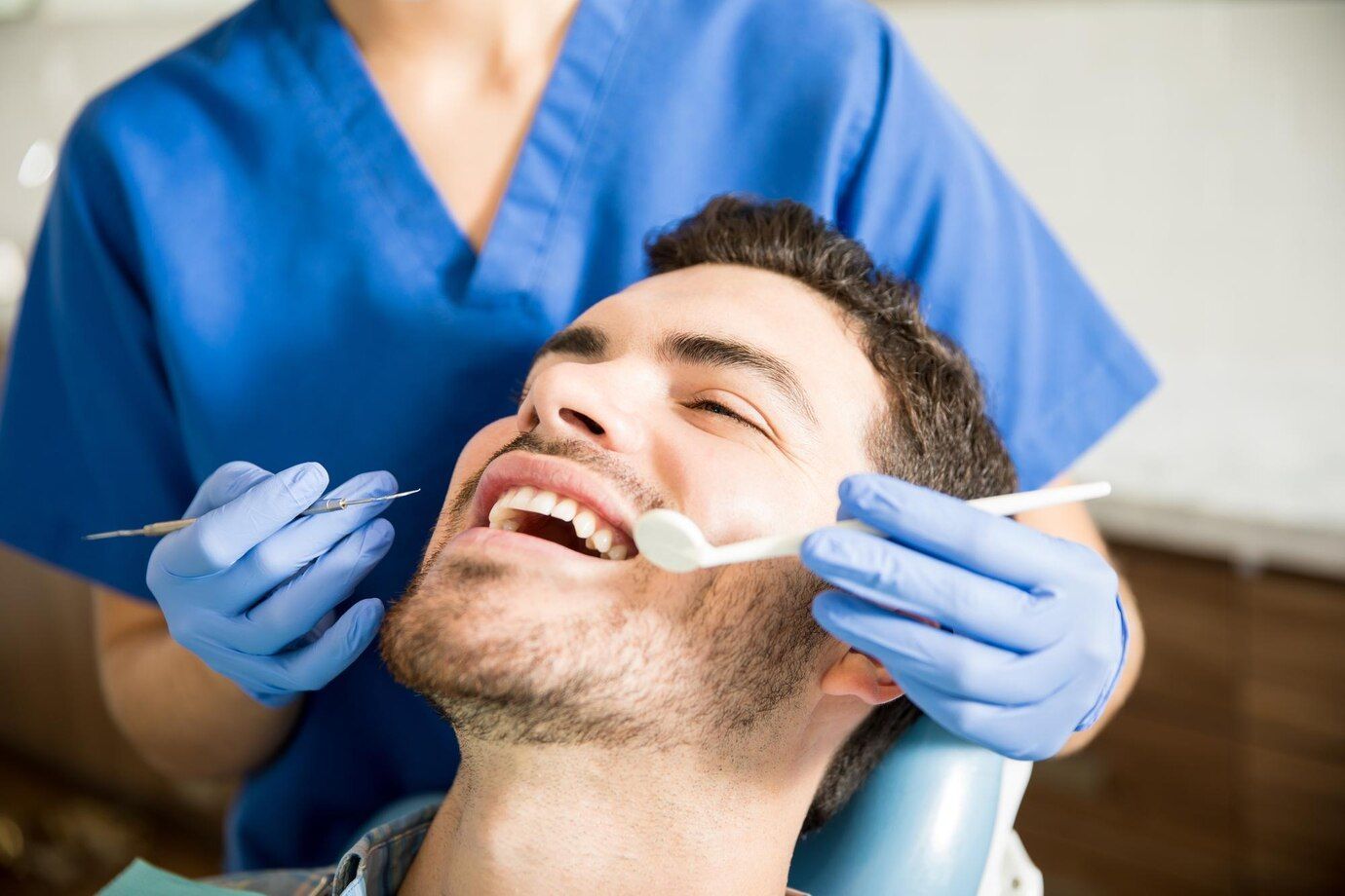 A man is sitting in a dental chair while a dentist examines his teeth.