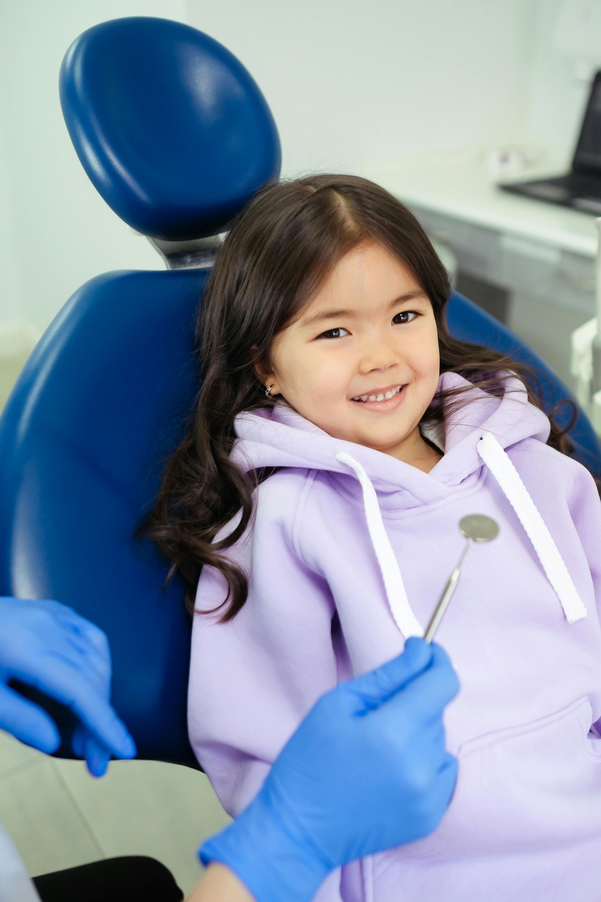 A little girl is sitting in a dental chair and smiling.