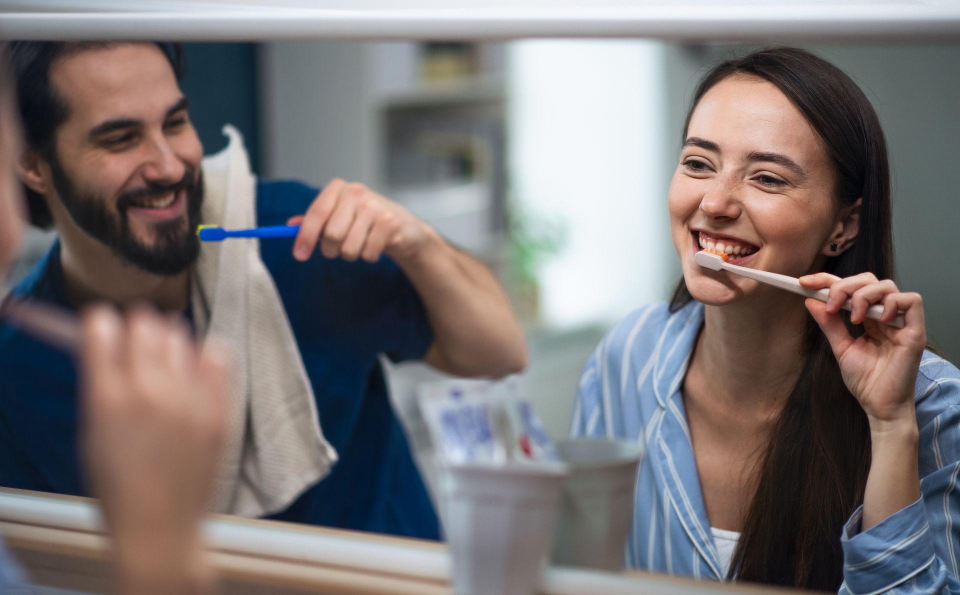 A man and a woman are brushing their teeth in front of a mirror.