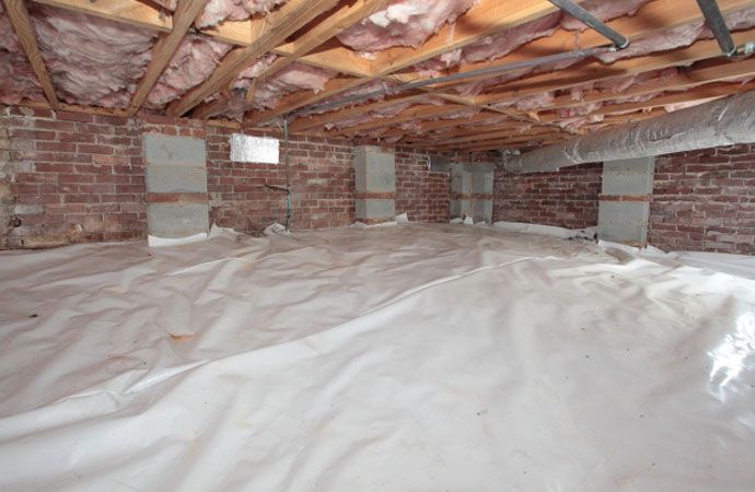 Crawl space with brick walls, insulation, and white vapor barrier on the floor.