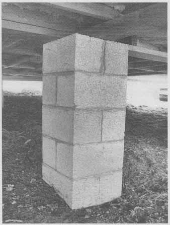 Concrete block pillar supporting a wooden structure, set in dirt.