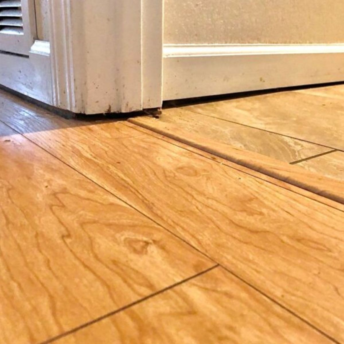 Warped laminate flooring abutting a doorway; the floor is wood-toned.