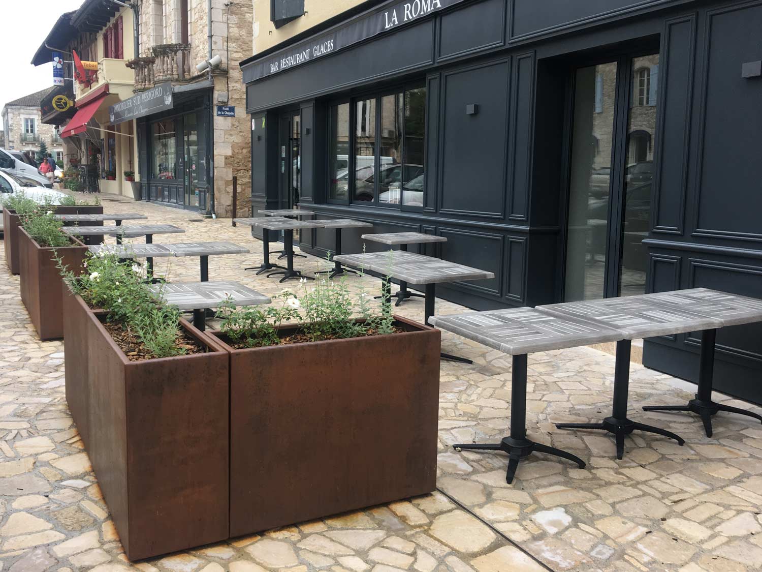 jardinières en acier corten dans rue piétonne délimitant la terrasse d'un restaurant