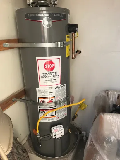 Gray water heater in a corner, with gas line and safety instructions.