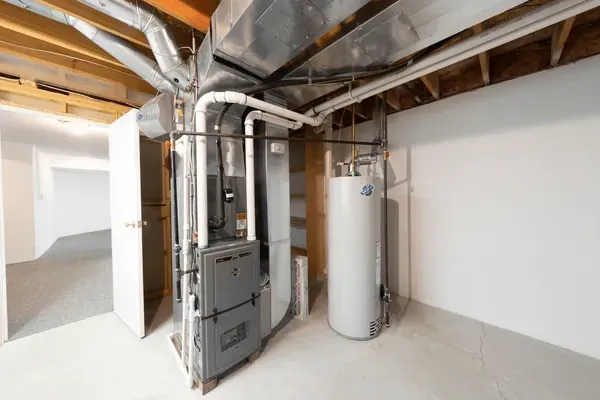 Basement with furnace, water heater, ductwork, and open door to a hallway with white walls and flooring.