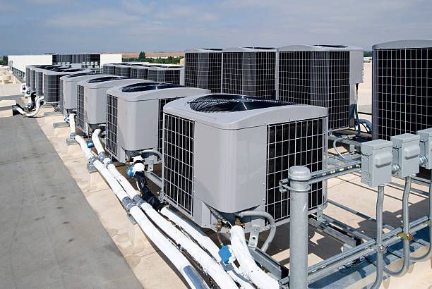 Air conditioning units aligned on a rooftop, with piping and electrical connections visible.