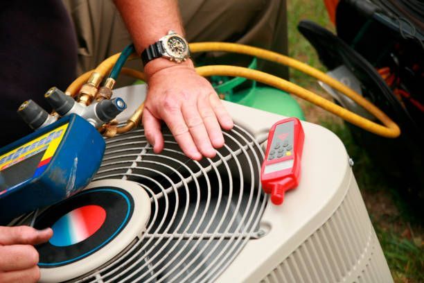 Person inspecting an air conditioning unit with gauges, hoses, and a digital thermometer.