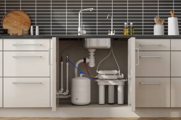Kitchen cabinet open, revealing a water filter system, pipes, and a tank below a sink.