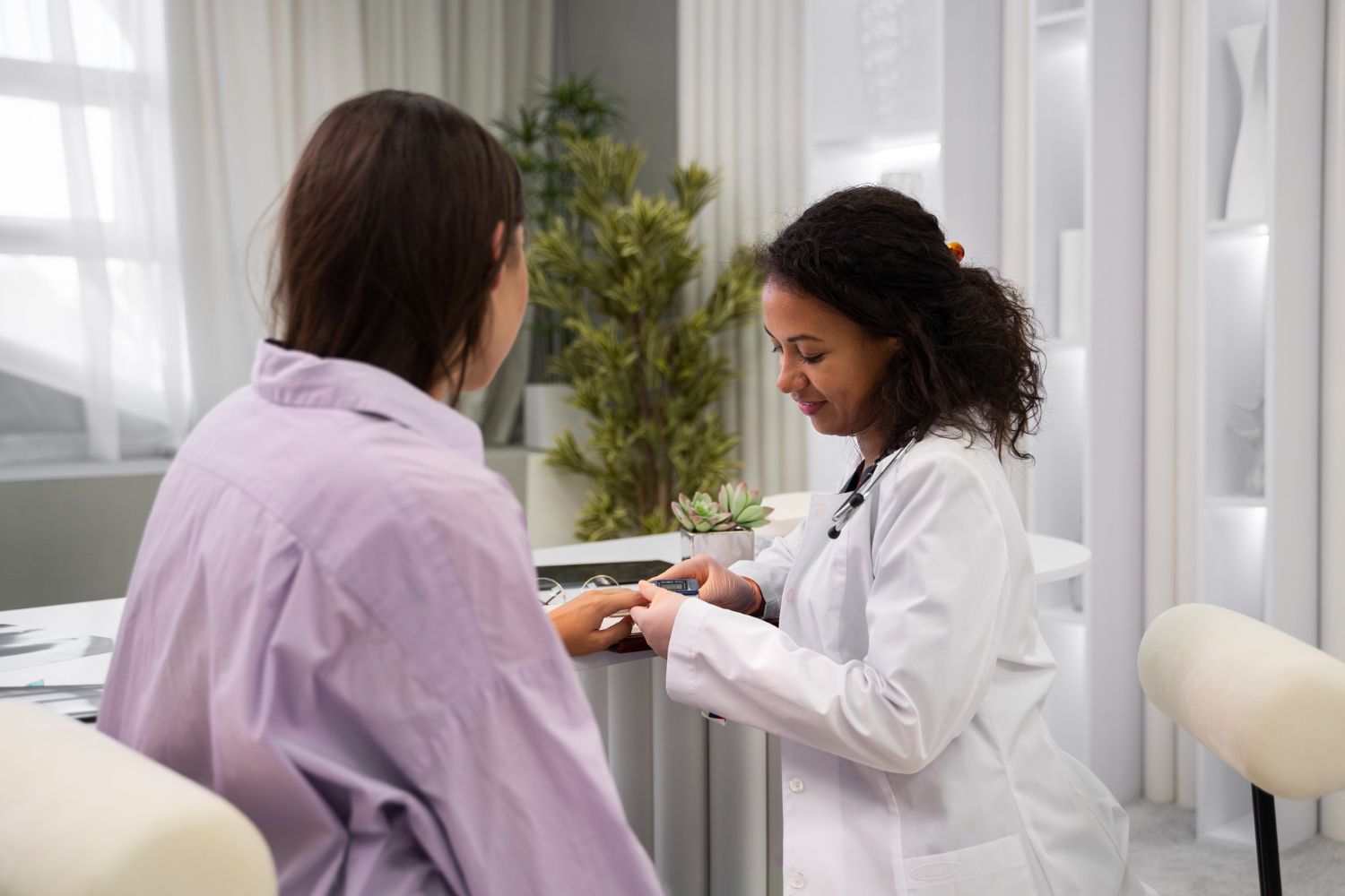 Doctor checking patient's wrist in a light-filled exam room. Both are smiling.