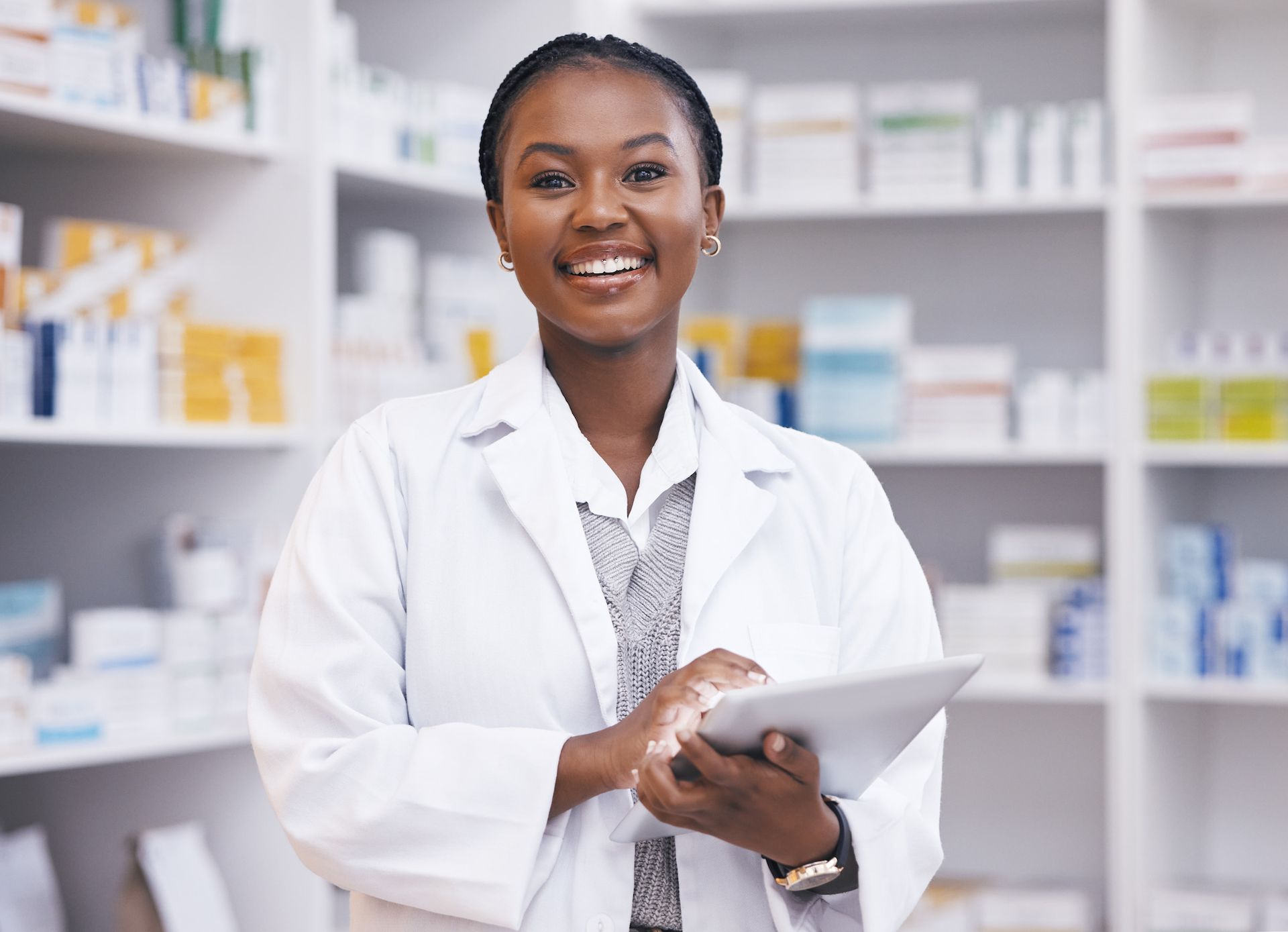 A female pharmacist is smiling while holding a tablet in a pharmacy.
