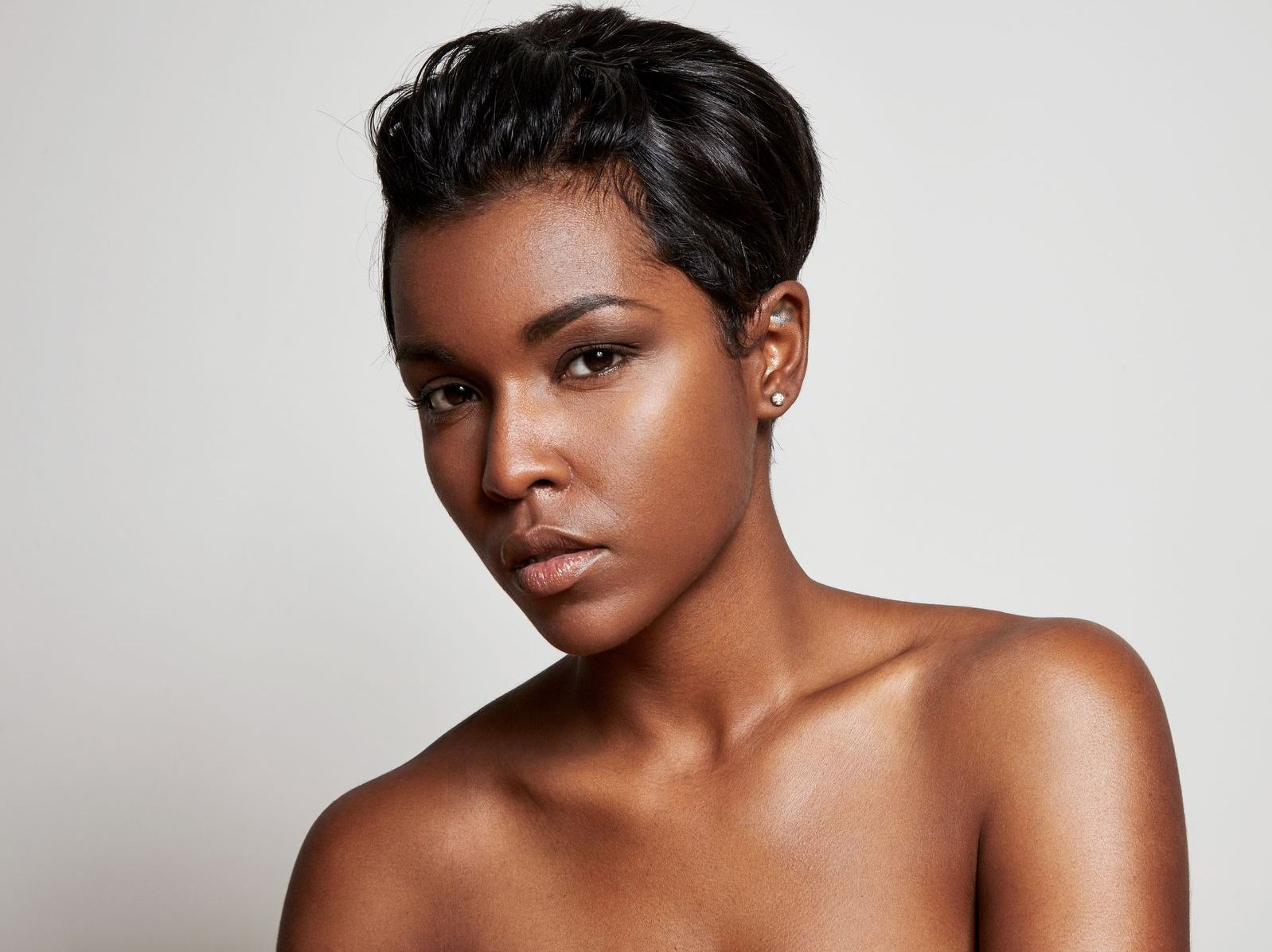 A shirtless woman with short hair is looking at the camera.
