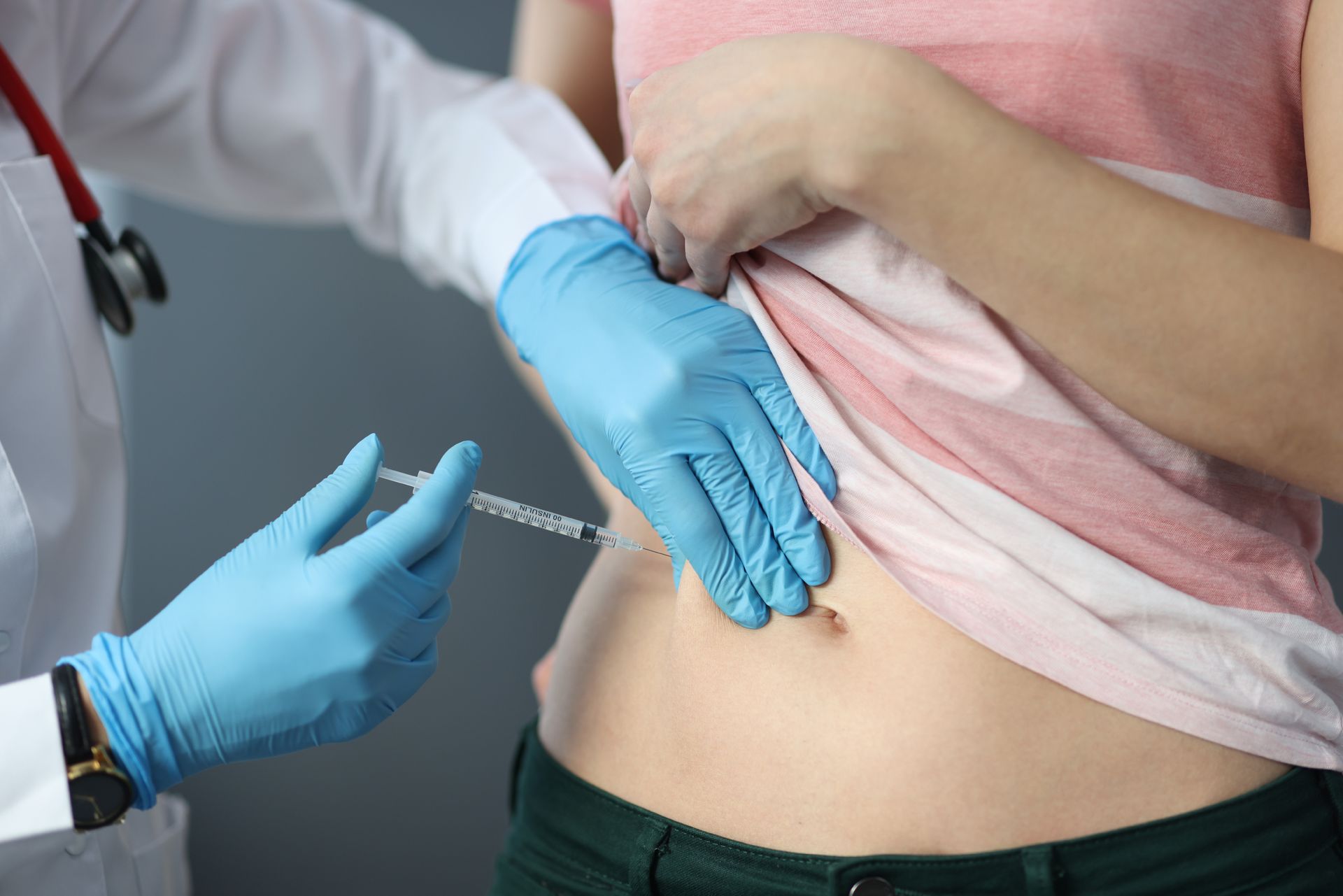 A doctor is giving a woman an injection in her stomach.
