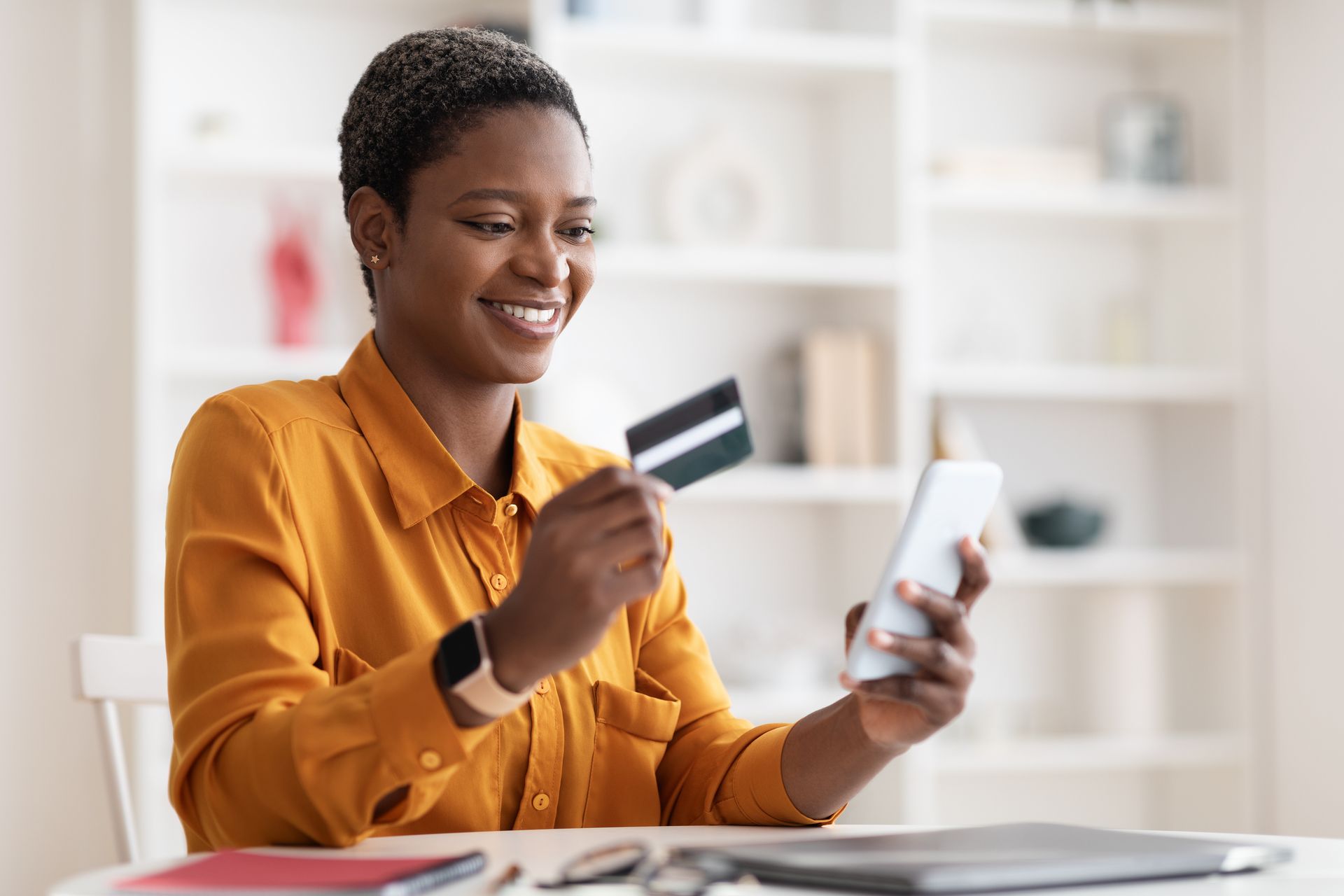A woman is holding a credit card and using a cell phone.