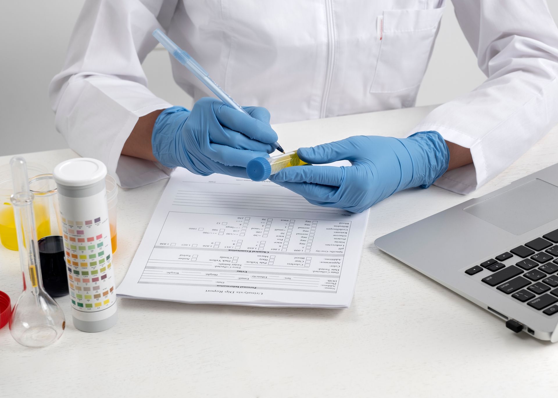 A scientist is sitting at a desk holding a test tube and writing on a piece of paper.