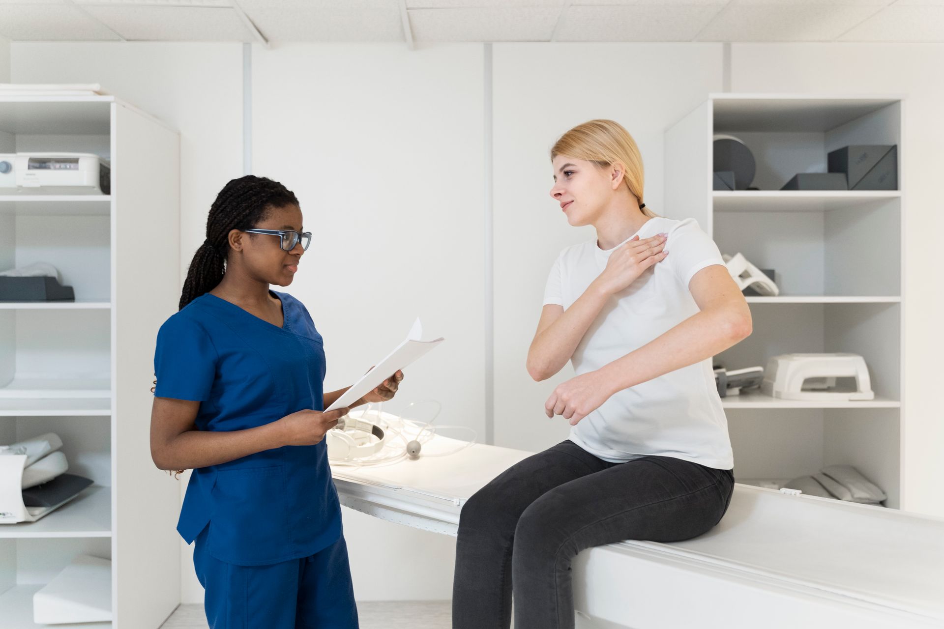 A nurse is talking to a patient who is sitting on a bed.