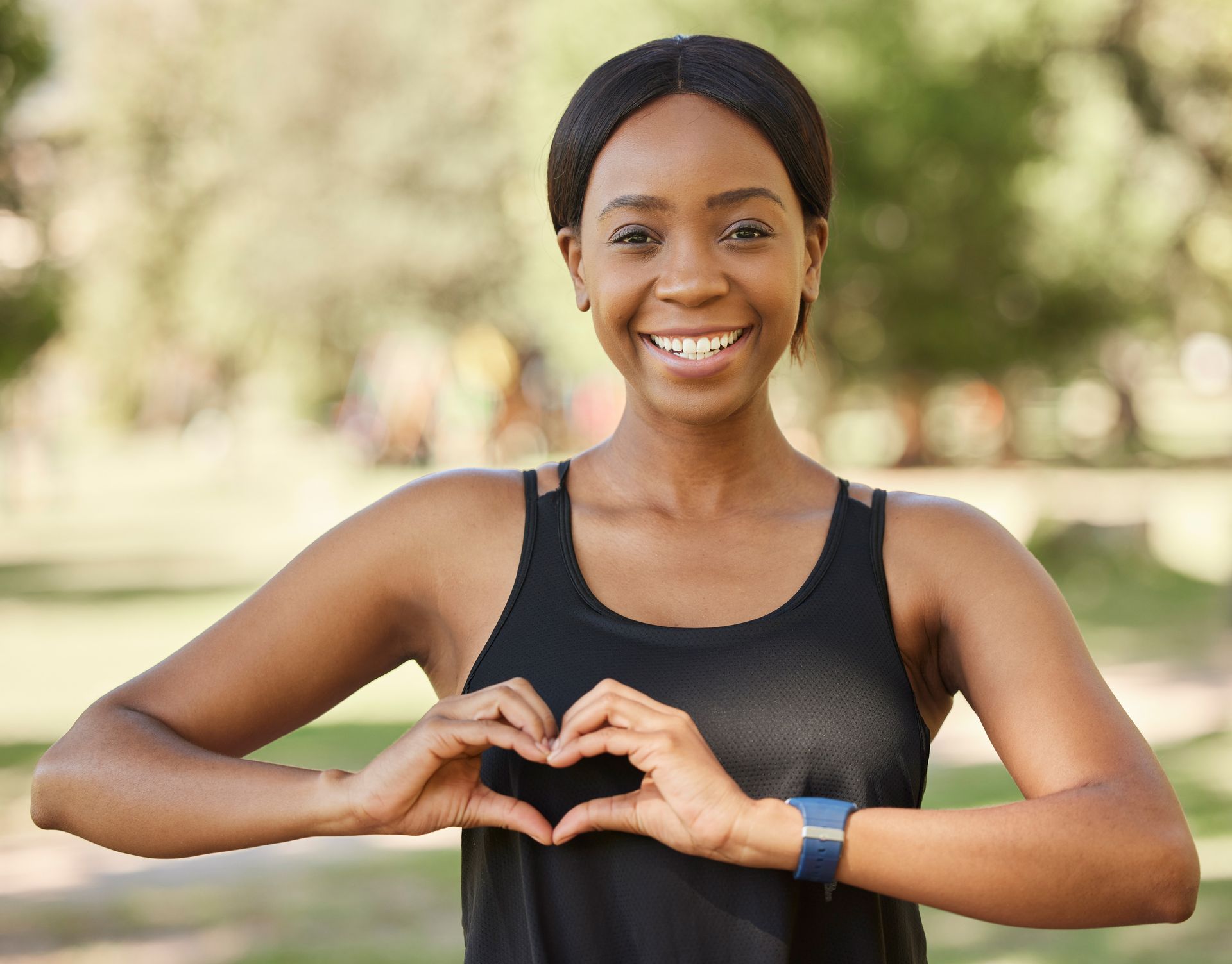 A woman is making a heart shape with her hands in a park.