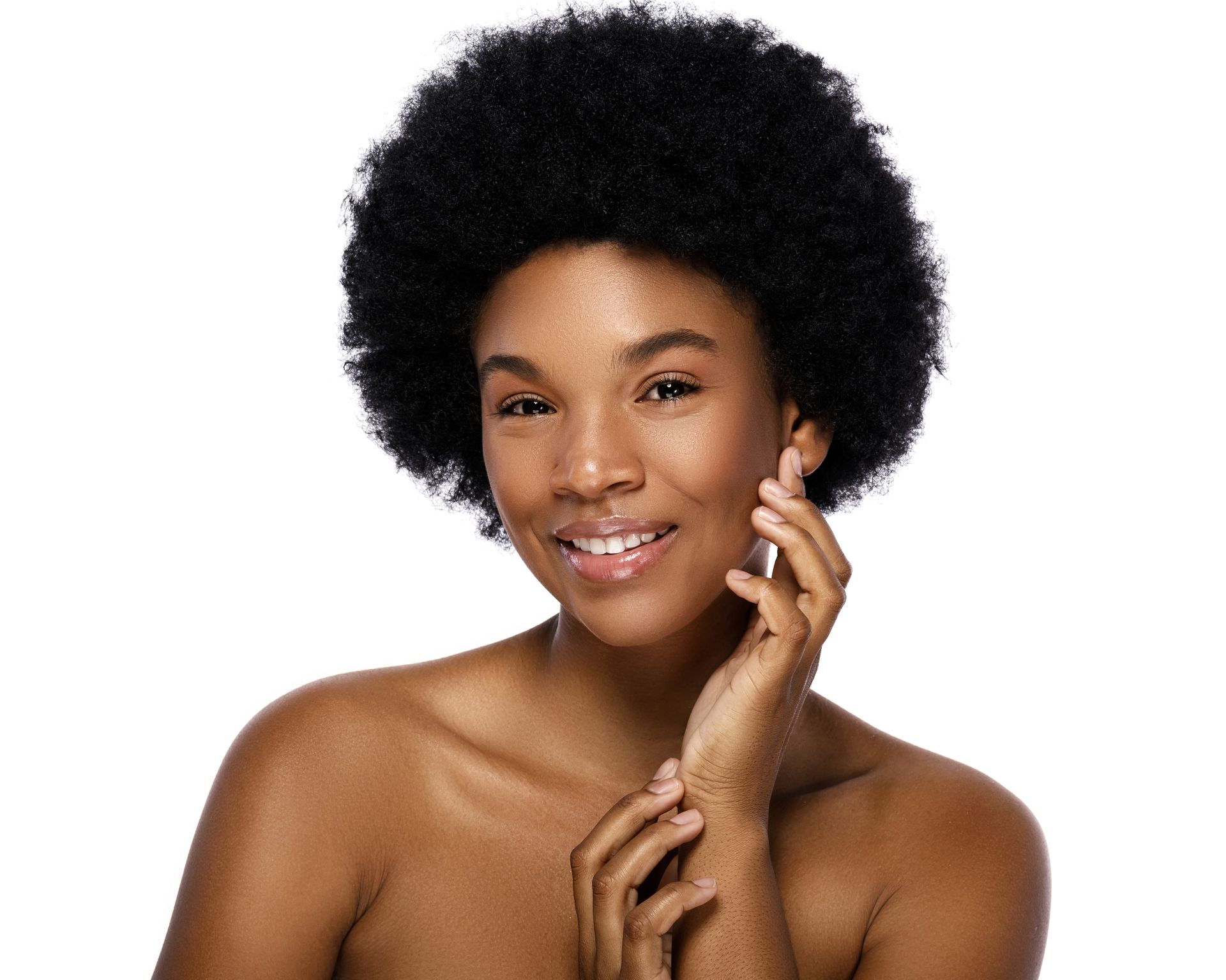 A woman with an afro is smiling and touching her face.