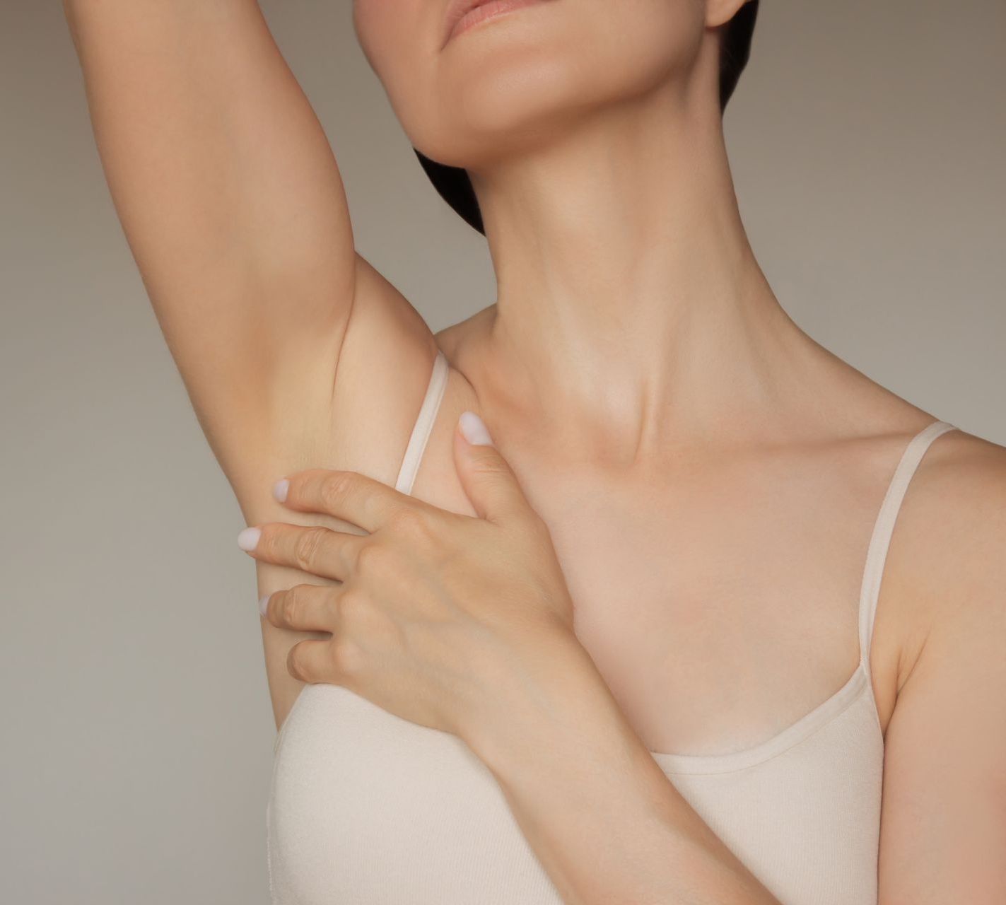A woman in a white tank top is holding her armpit.