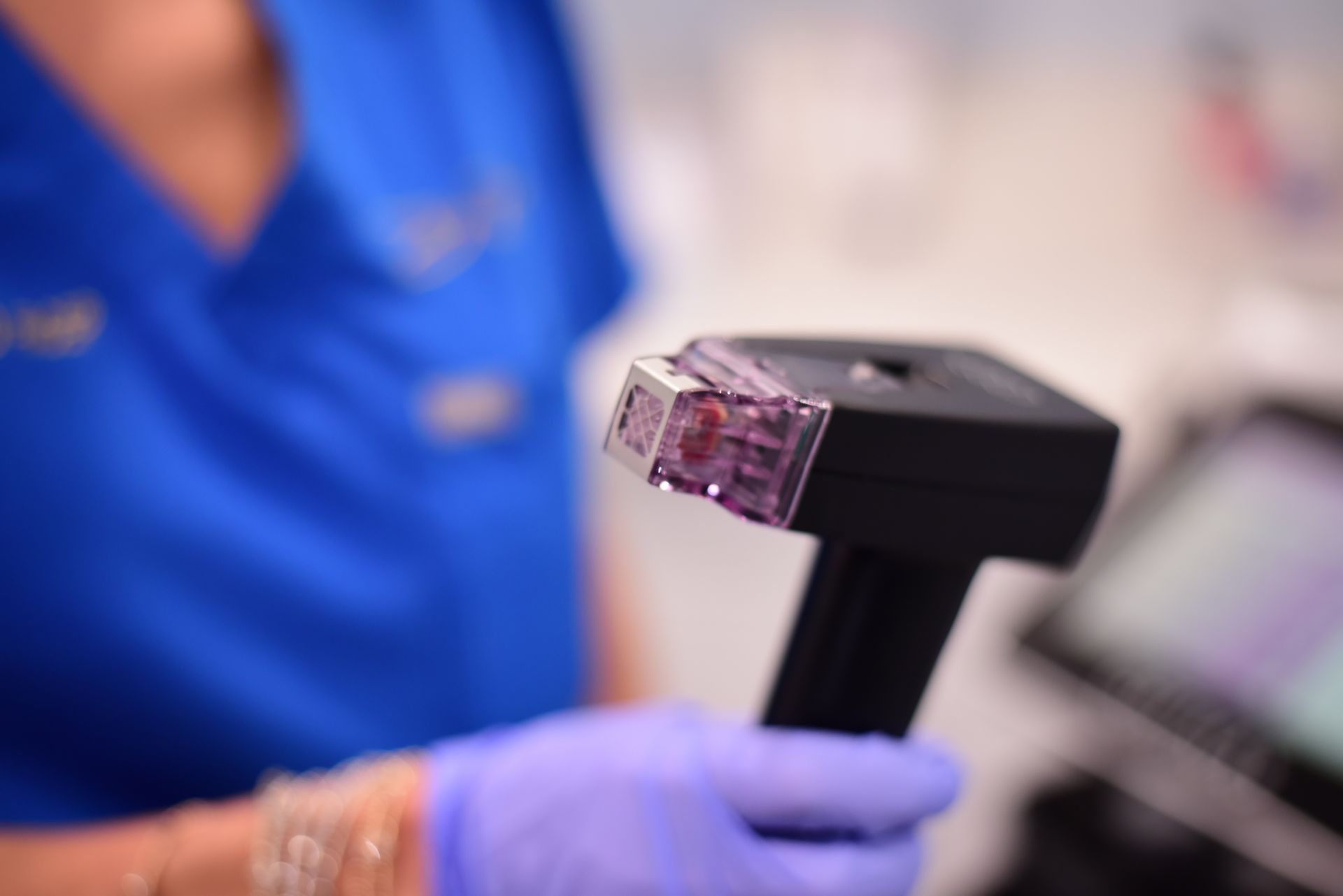 A person wearing purple gloves is holding a device in their hand.