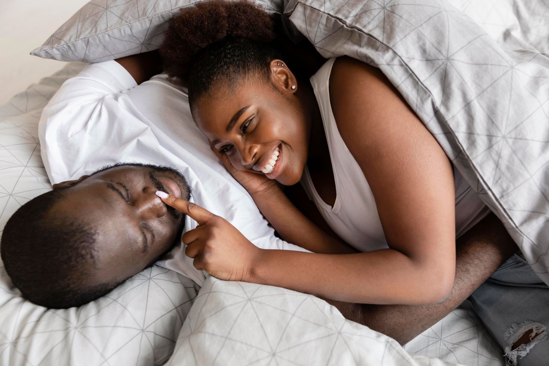 A man and a woman are laying in bed under a blanket.
