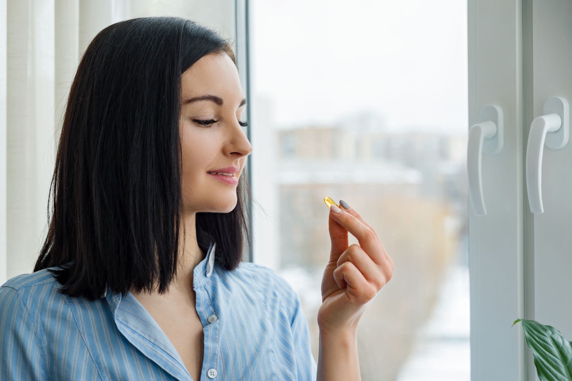 A woman is taking a pill in front of a window.
