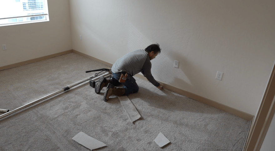 Worker installing carpet in an empty room, kneeling on the floor with tools nearby.