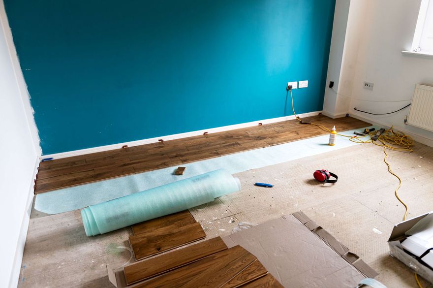 Renovated room with teal accent wall, wood flooring, rolled-up carpet, and scattered tools on the floor