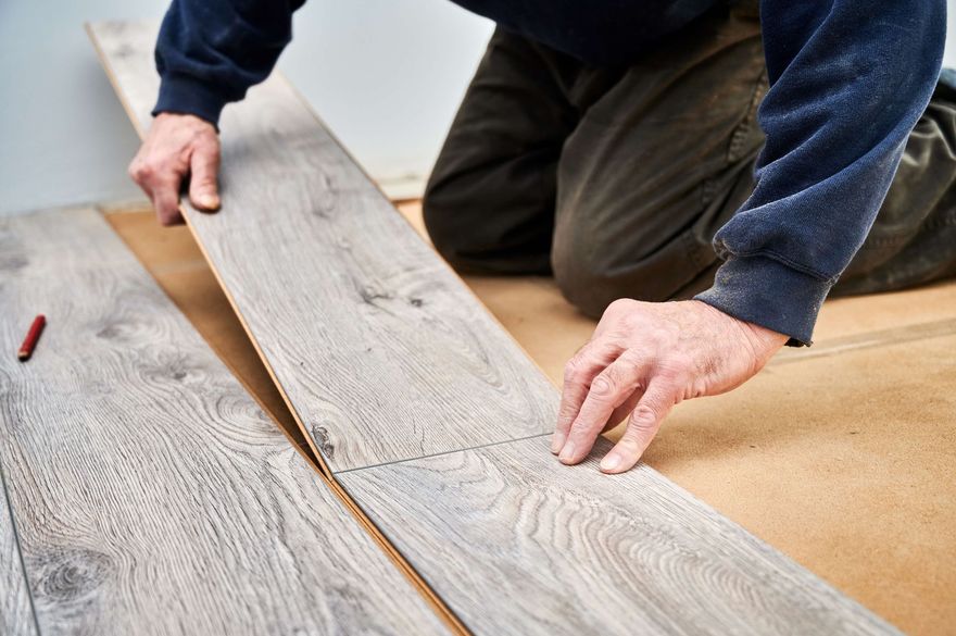 Hands installing gray wood flooring with a measuring tool nearby