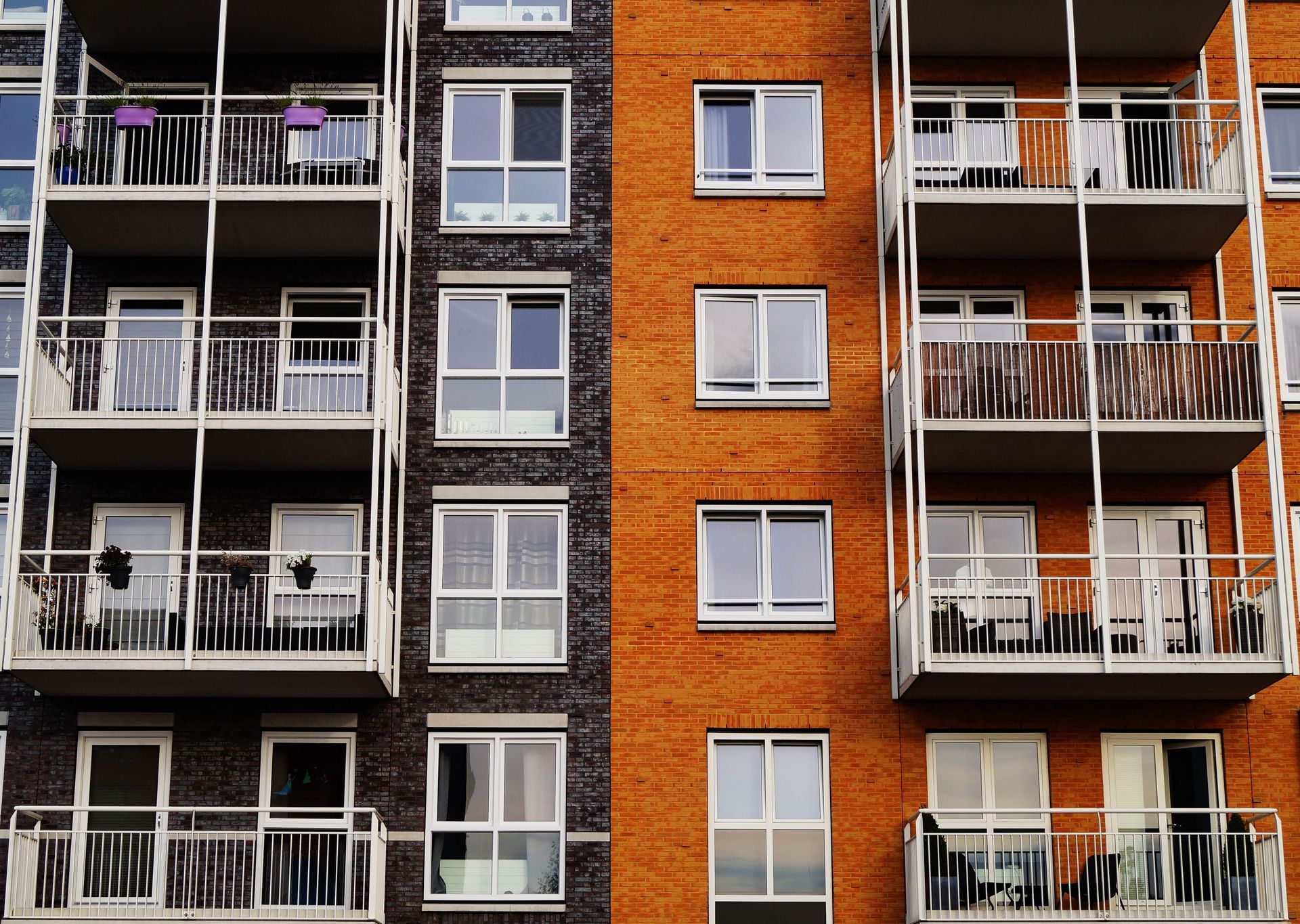 Apartment building facade with orange brick and white balconies, featuring rows of windows and gray siding