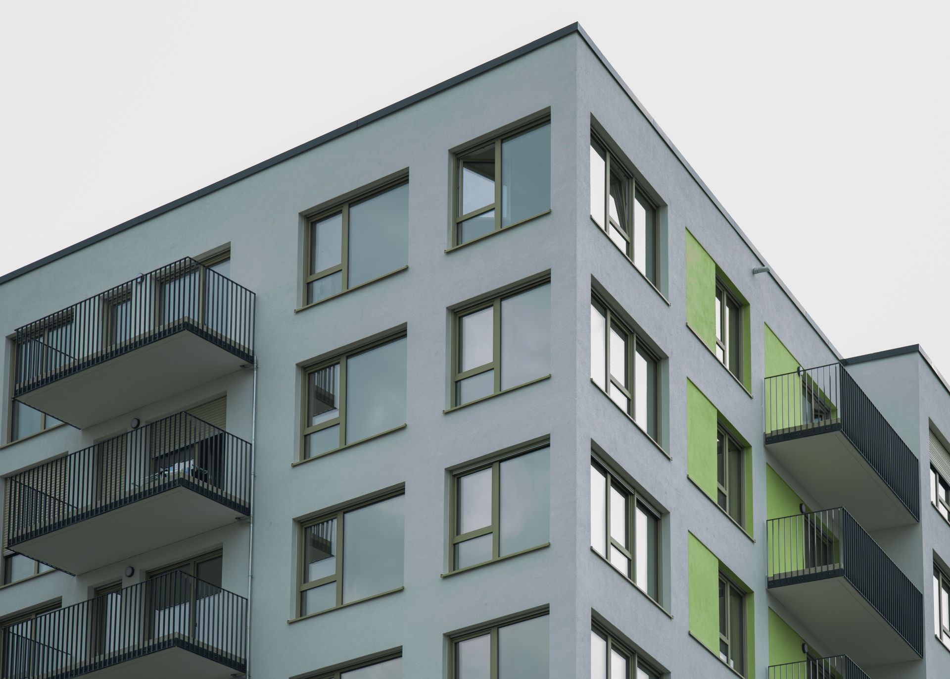 Modern apartment building with gray and green facades and balconies against a cloudy sky
