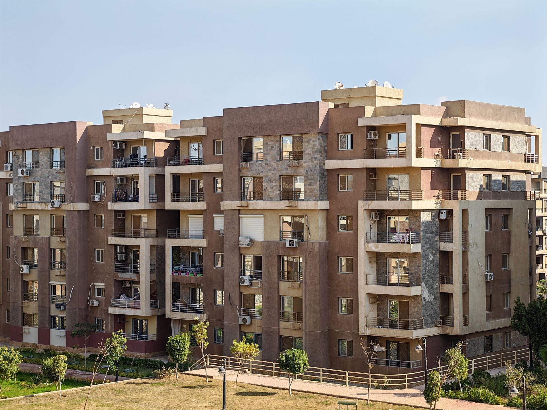 Modern brown apartment buildings with balconies and balconies, surrounded by greenery under a clear sky