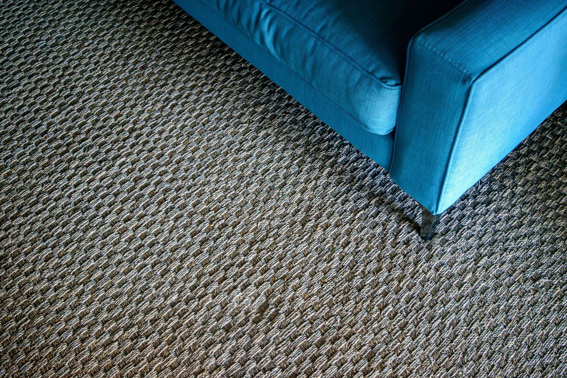 Blue upholstered sofa corner on a gray patterned carpet.