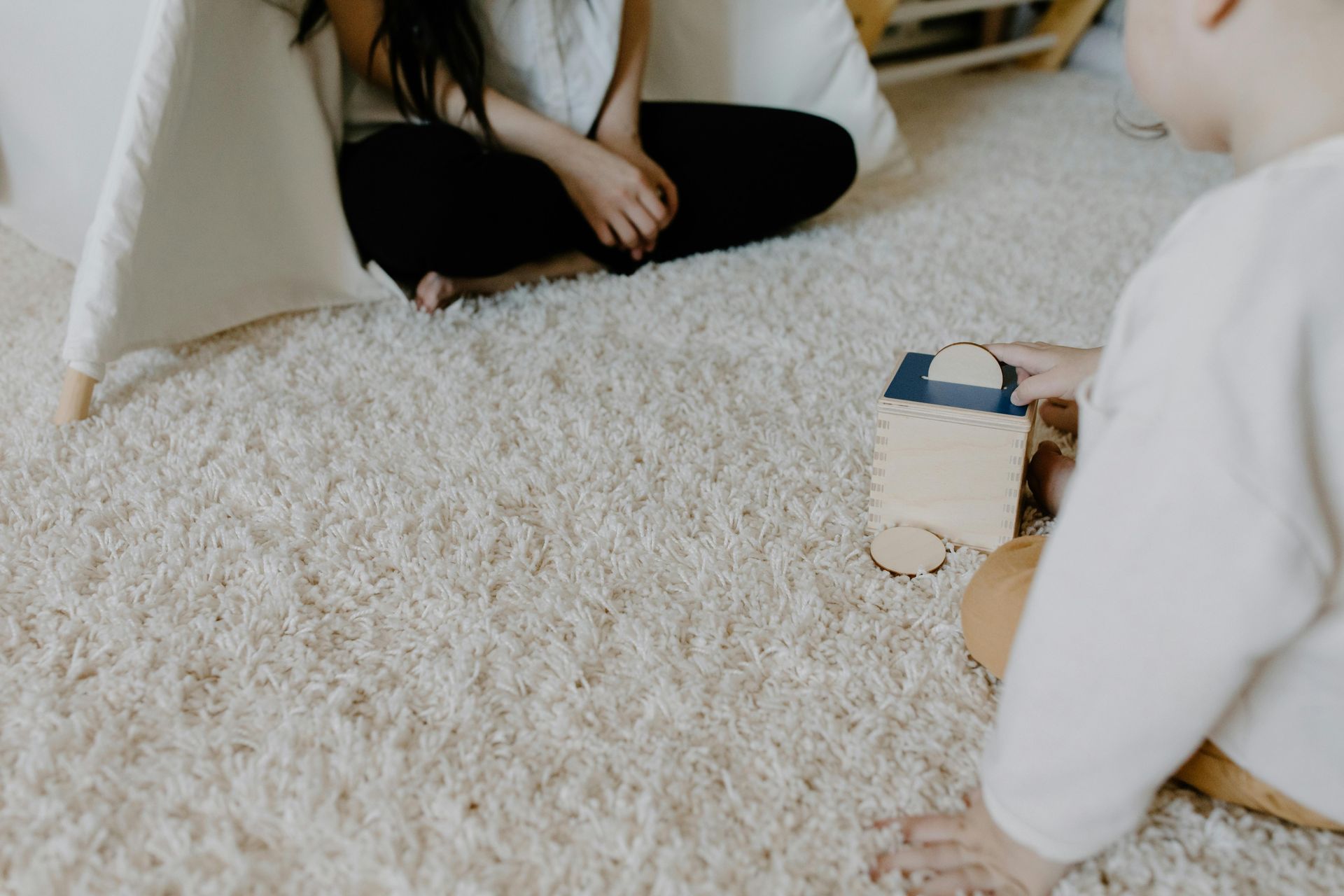 People sitting on a white shag rug, playing with a small toy block.