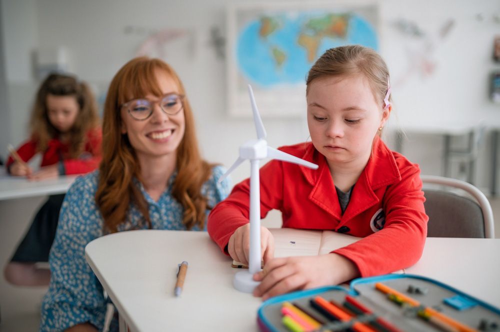 Down Syndrome Schoolgirl With Model Of Wind Turbine With Help Of Teacher Learning About Eco-friendly Renewable Sources Of Energy In Class At School — Child Inclusive Dispute Resolution in Kingscliff, NSW