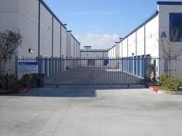 A gated driveway leading to a warehouse with a fence.