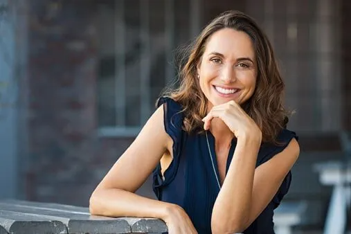 A woman is leaning on a railing and smiling.